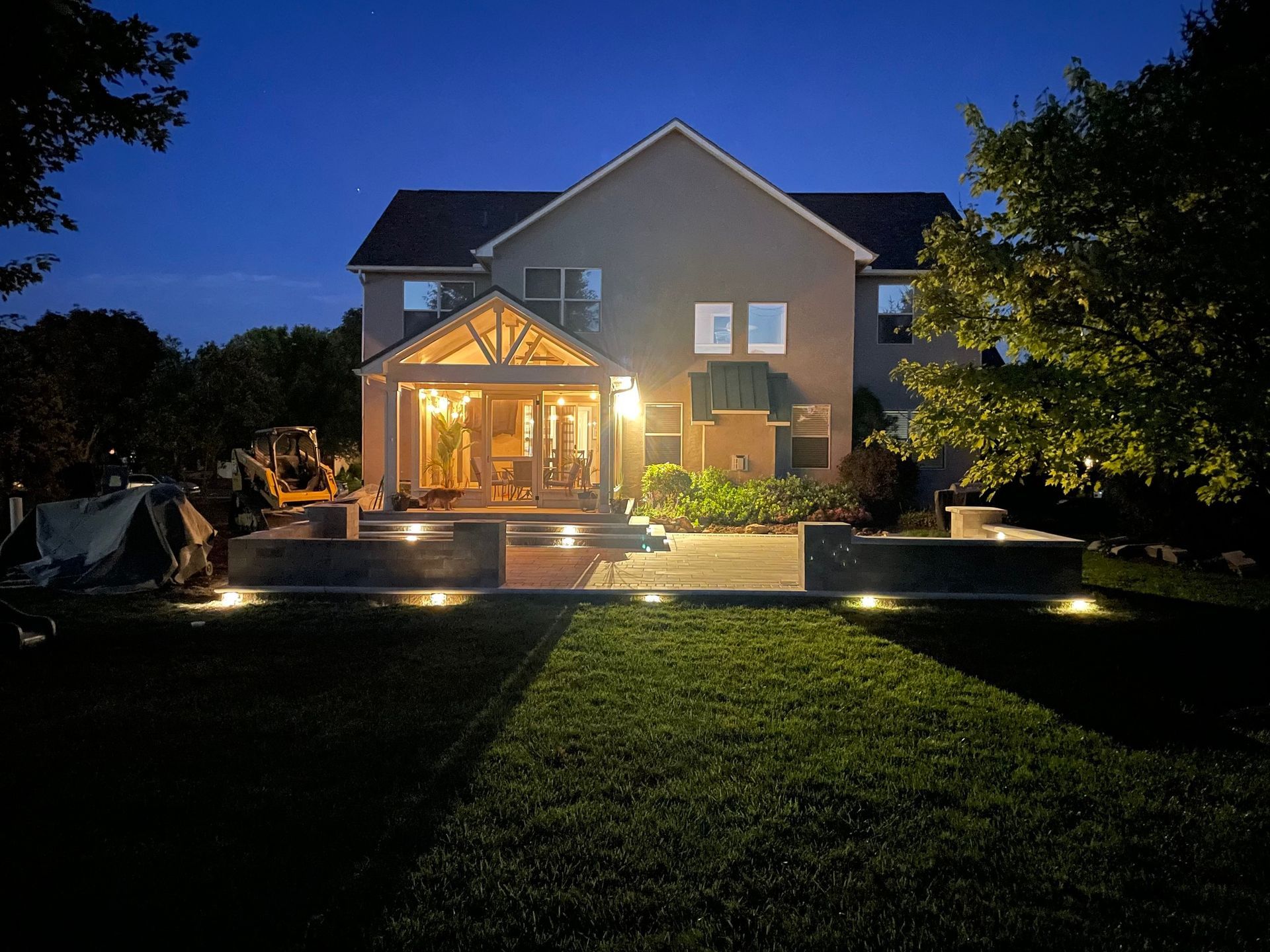 Night shot of a two-story house with a lit patio, grassy yard, and landscape lighting.