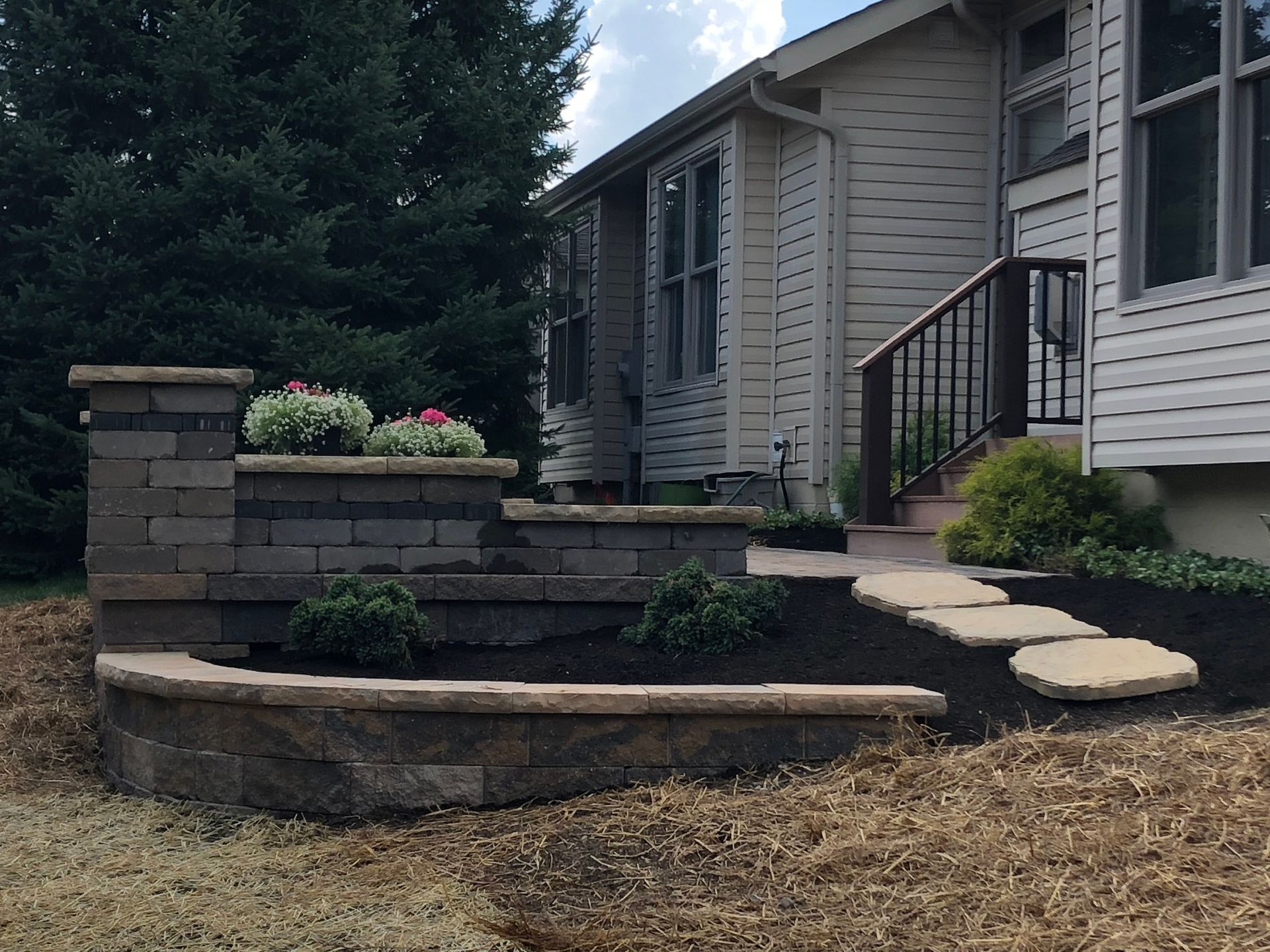 A brick retaining wall with steps leading to a house entrance, with plants and landscaping.