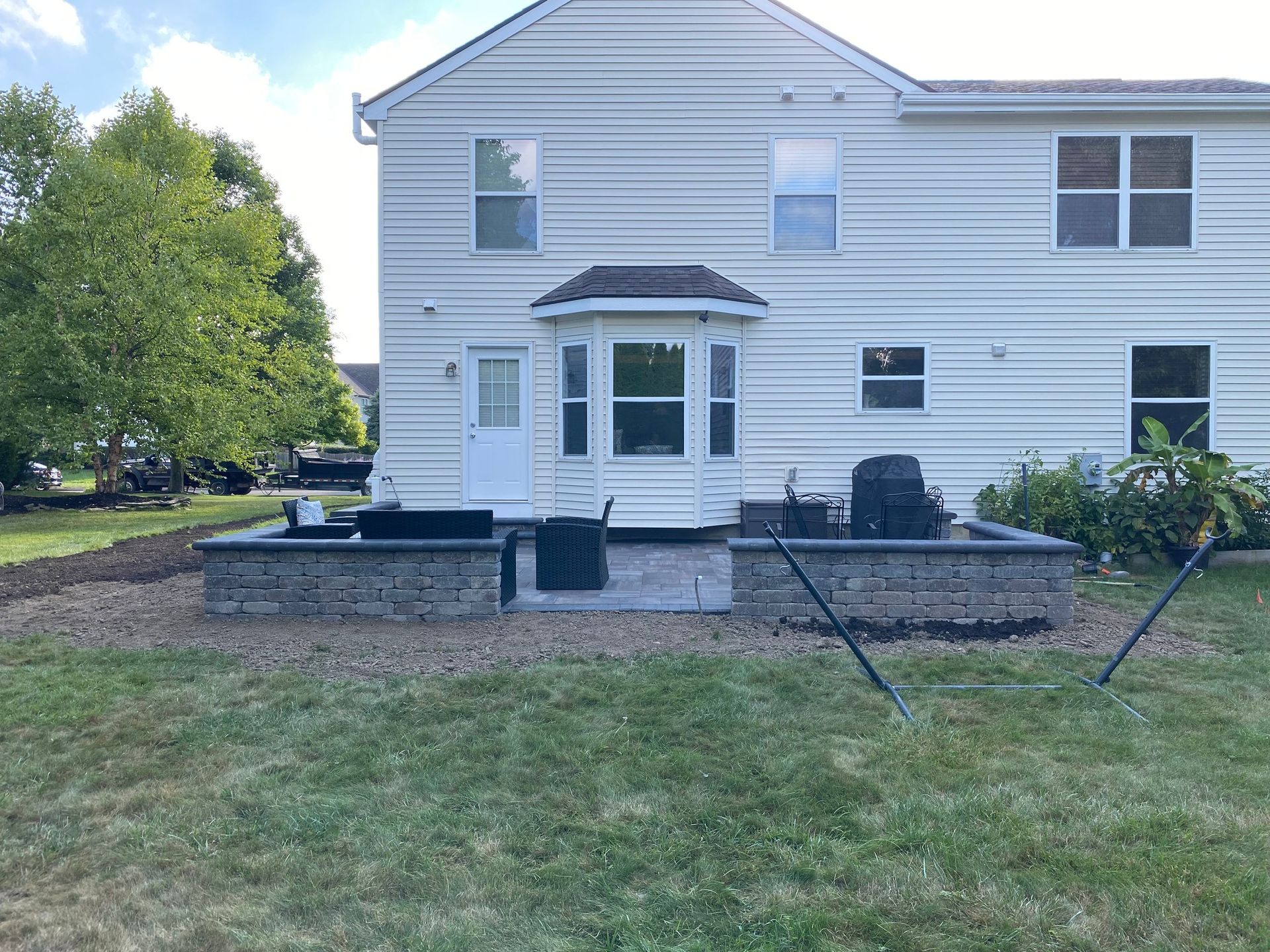 Backyard patio with raised stone beds in front of a two-story house.