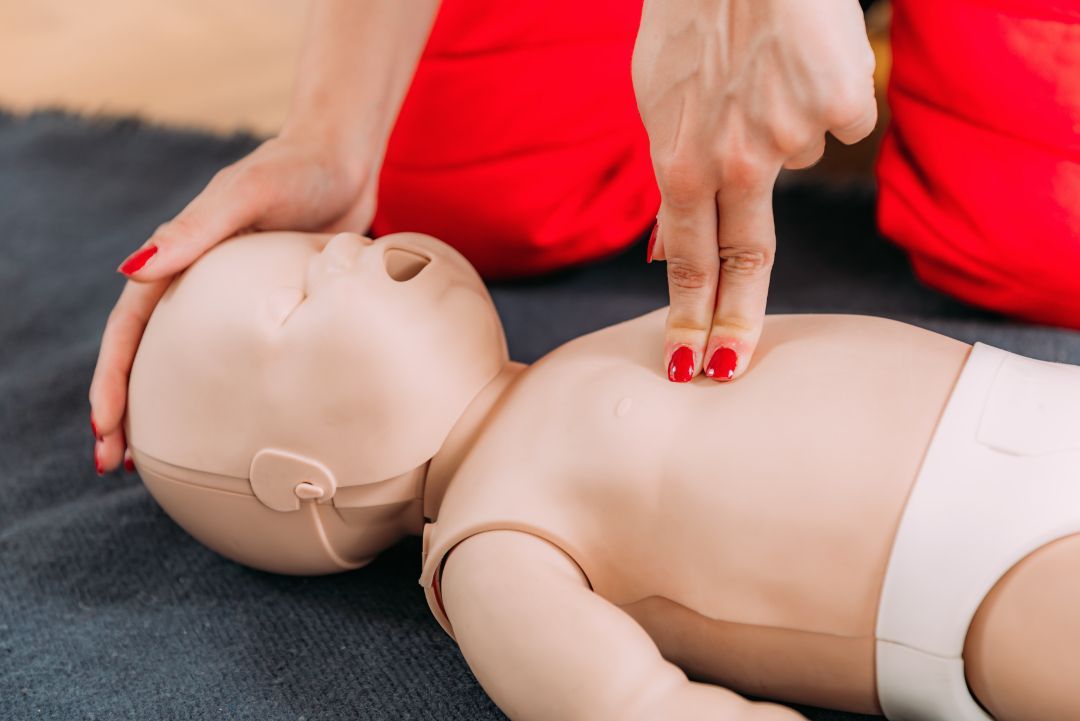 A woman is practicing first aid on a baby mannequin.