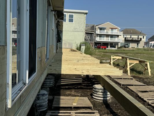 Construction of a wooden deck and steps next to a house, with concrete supports and nearby houses.