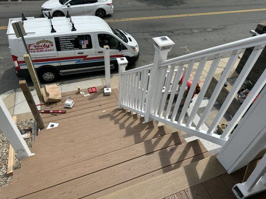 White railing and stairs on a deck with a commercial van parked nearby on a street.