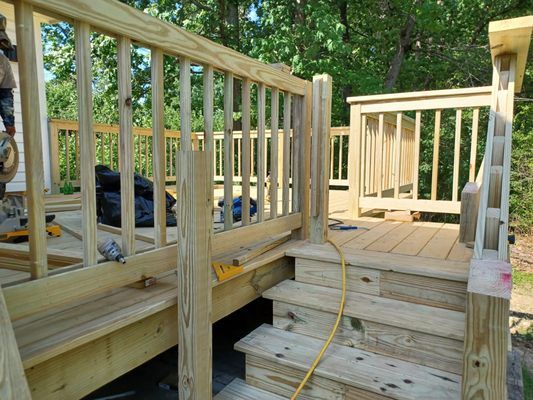 Wooden deck with stairs, railing, and a section of bench seating, outdoors.