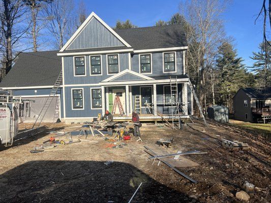 Blue house under construction on a sunny day with tools and ladders scattered.