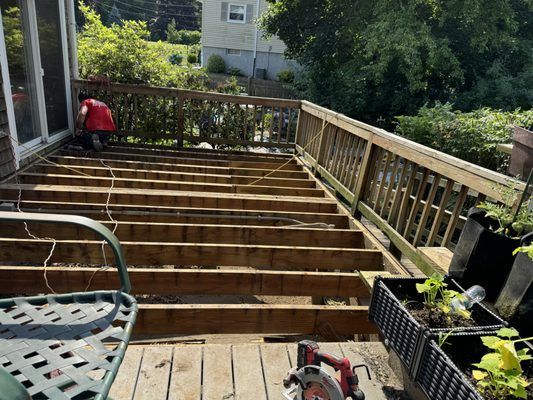 Deck under construction; worker in red shirt, removed decking, wooden railings, outdoor setting.