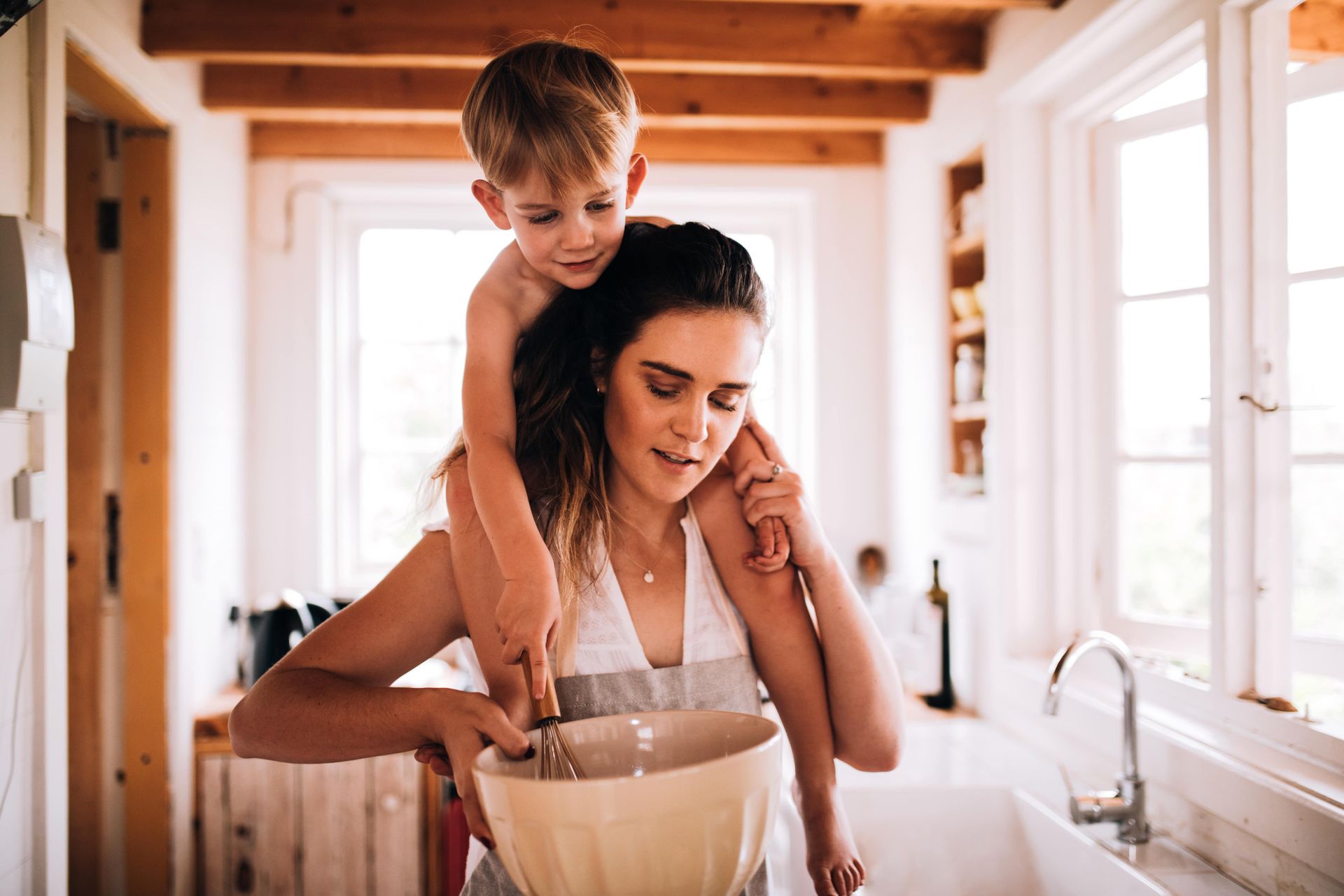 A woman is holding a little boy on her shoulders in a kitchen.