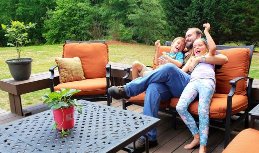 A man and two children are sitting on a couch on a deck.