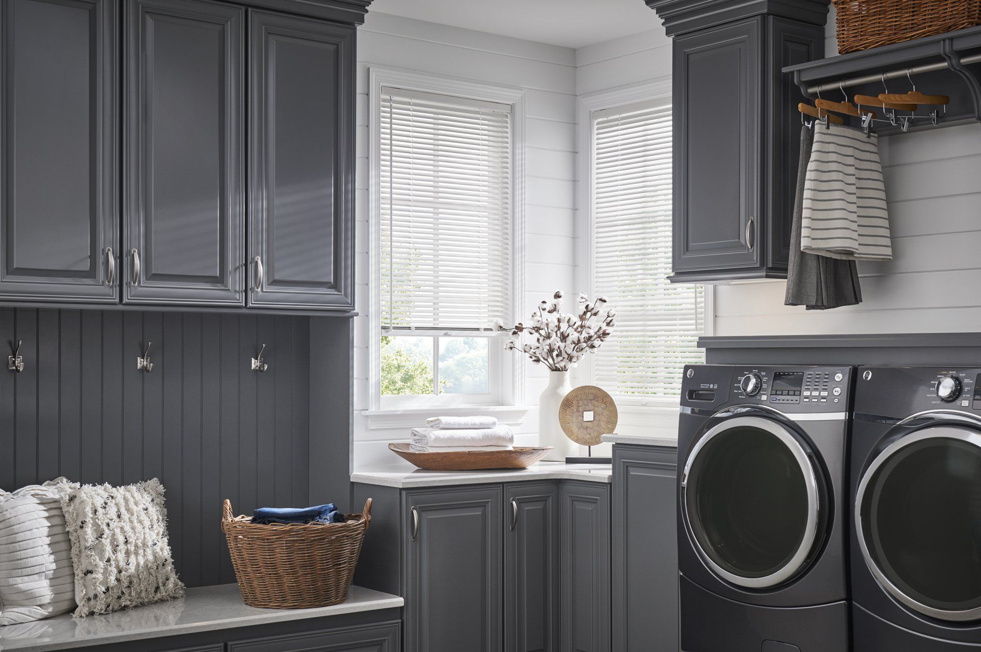 A laundry room with gray cabinets , a washer and dryer , and a window.