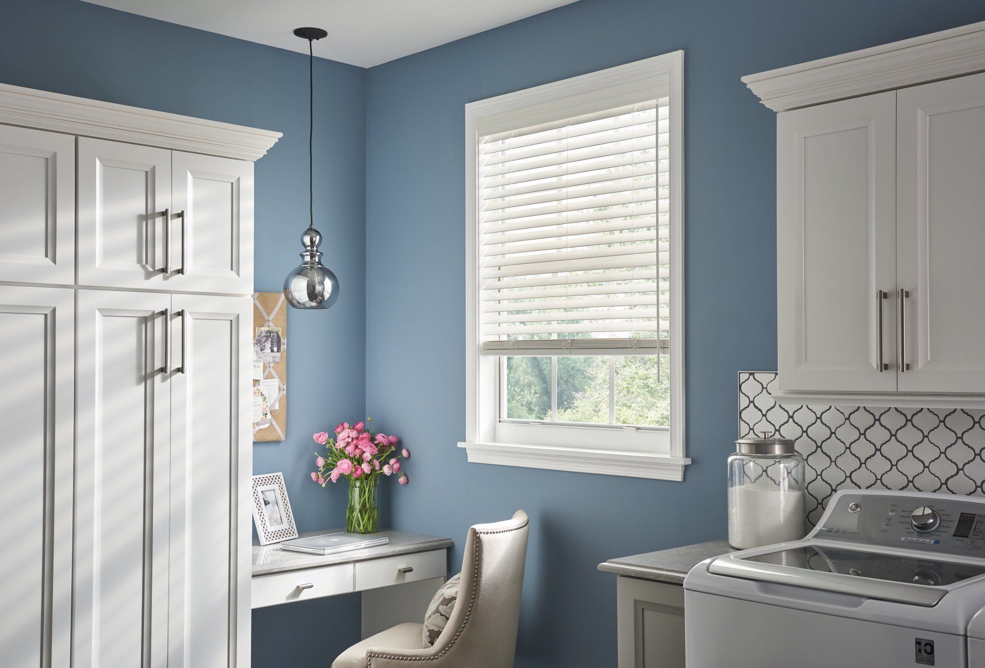 A laundry room with blue walls , white cabinets , a washer and dryer , and a window.