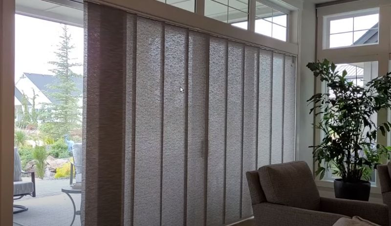 I living room with large sliding glass doors has panel track shades. 