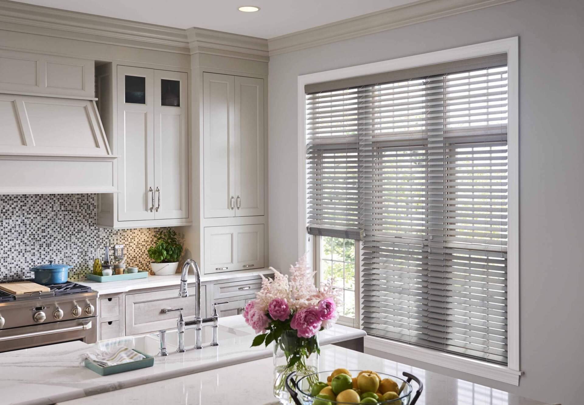 A kitchen with white cabinets , a stove , a sink , and a window with blinds.