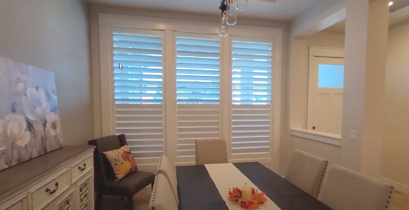 A dining room with a table and chairs and shutters on the windows.