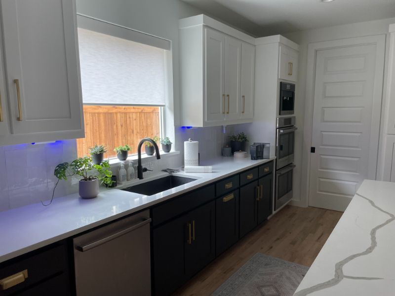 A kitchen with white cabinets , black cabinets , a sink , and a window.