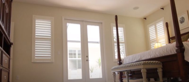 A bedroom with a four poster bed , a bench , and a sliding glass door.