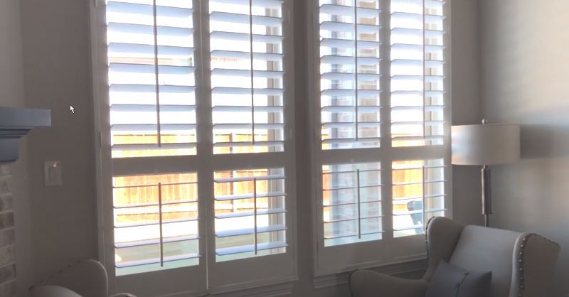 A living room with a couch , chair , lamp and shutters on the windows.