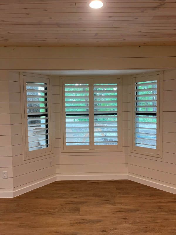 A room with a bay window and shutters on the windows.