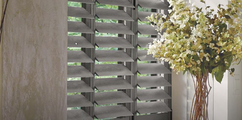 A vase of flowers is sitting in front of a window with shutters.