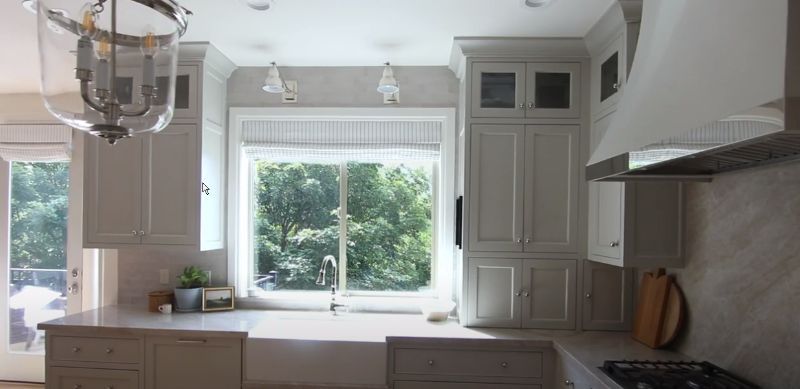 A kitchen with white cabinets , a sink , a stove , and a window.