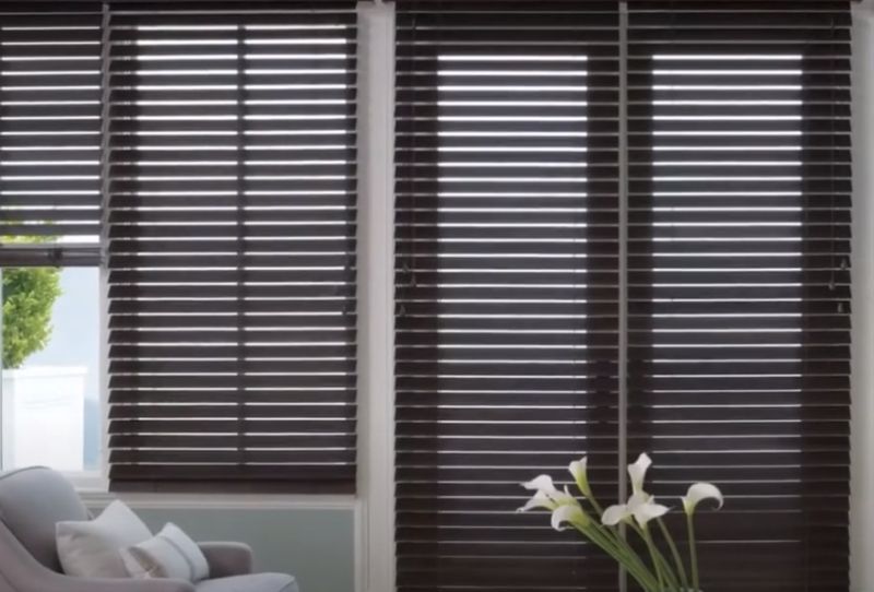 A living room with a couch and a vase of flowers in front of a window with blinds.