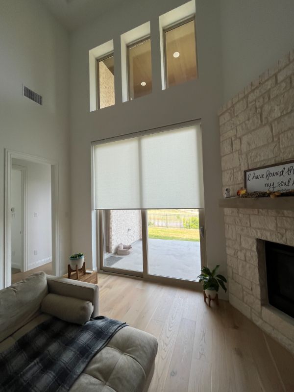 A wall of windows new to a fireplace has roller shades. 