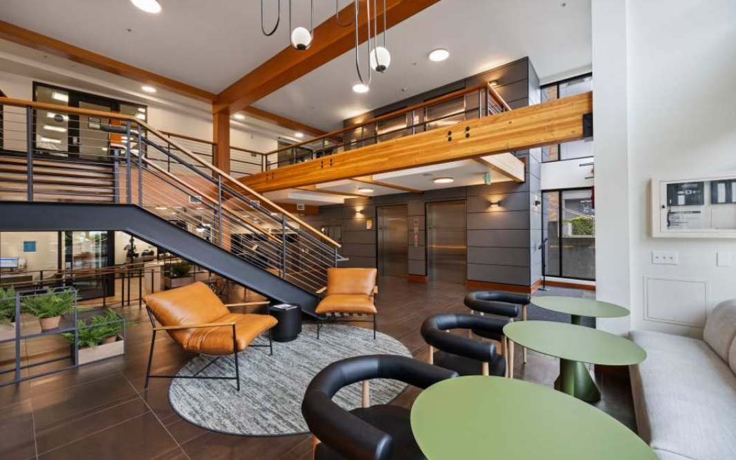 Lobby with seating, staircase, and wood beams.  Modern design with green tables, brown leather chairs, and plants.