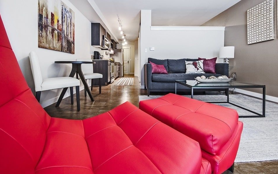Modern living space with red chair, gray couch, small kitchen, and artwork.