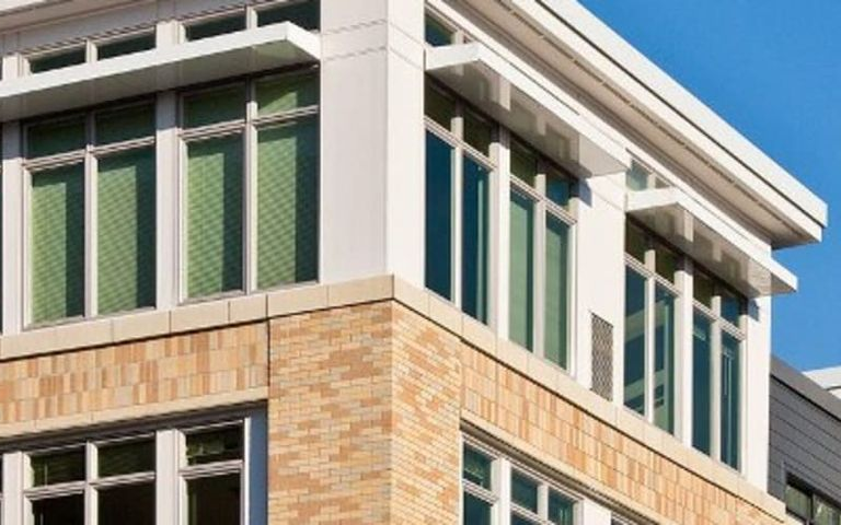 Modern building with tan and gray facade against a clear blue sky.