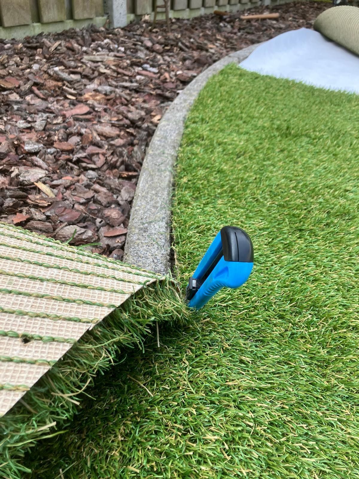 Blauw stanleymes snijdt groen kunstgras langs een grindrand.