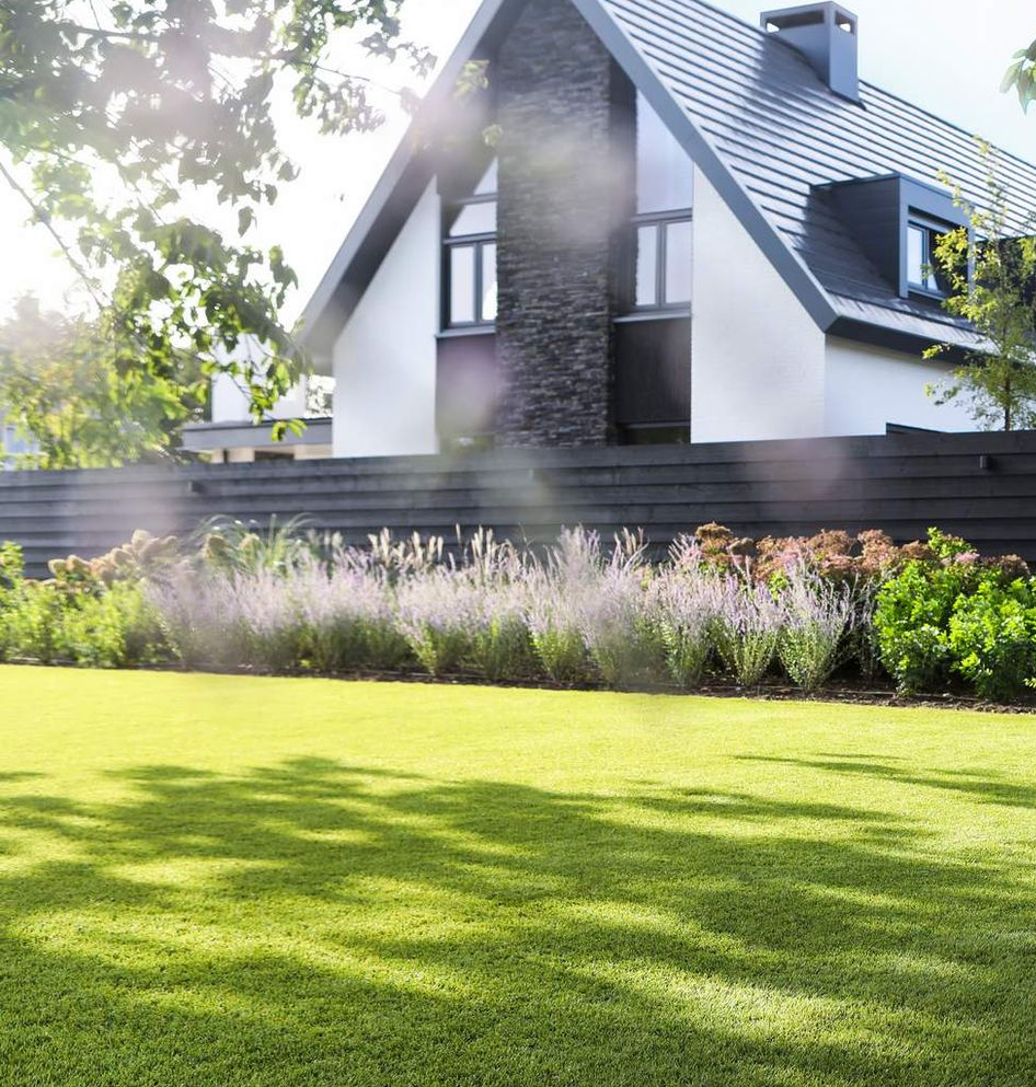 Een wit huis met twee verdiepingen, een donker dak en een goed onderhouden, groen gazon.