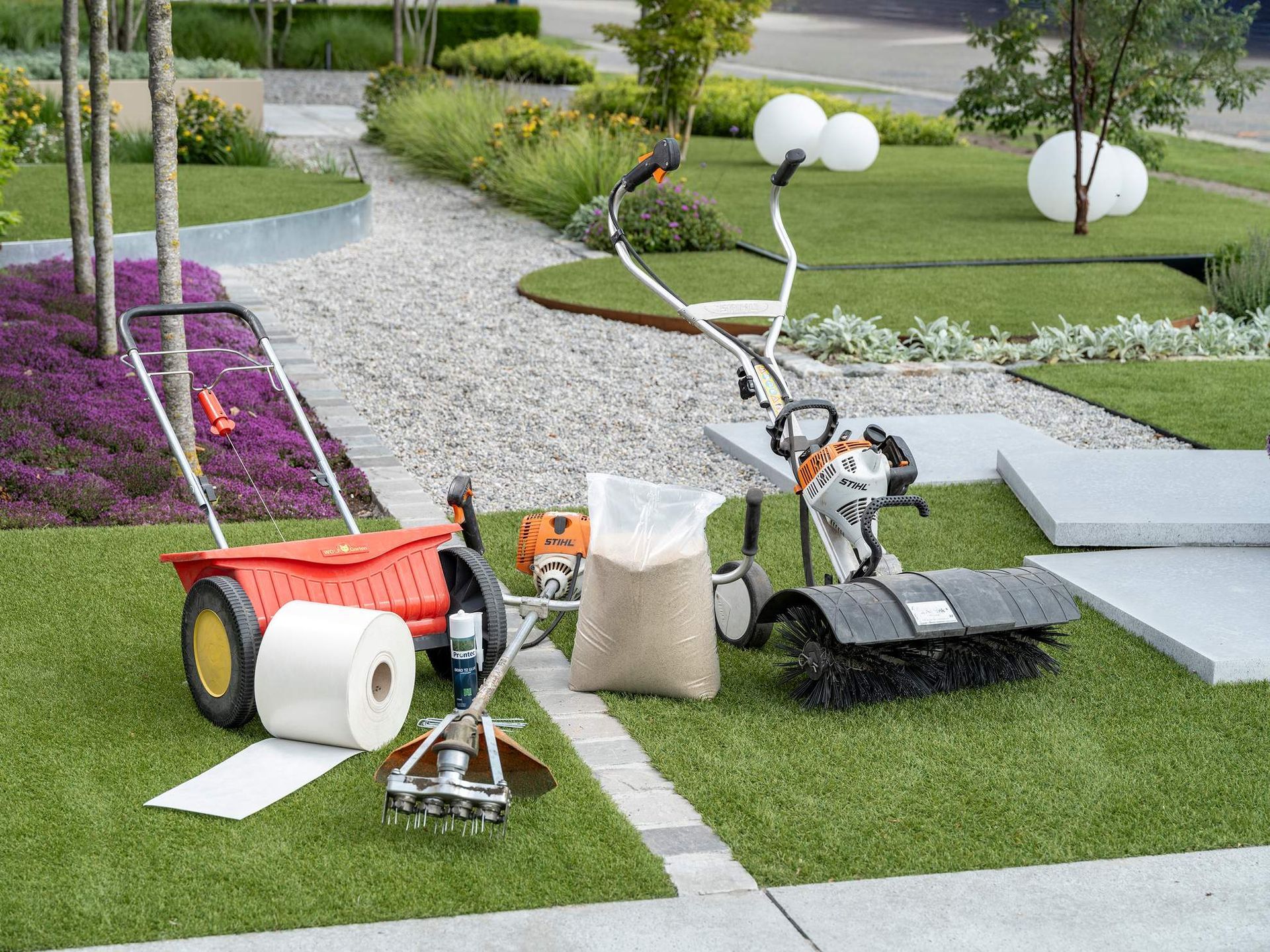 Gereedschap voor het onderhouden van gazons op groen gras: grasmaaier, zaaimachine, beluchter, borstel en rol papier, buiten.