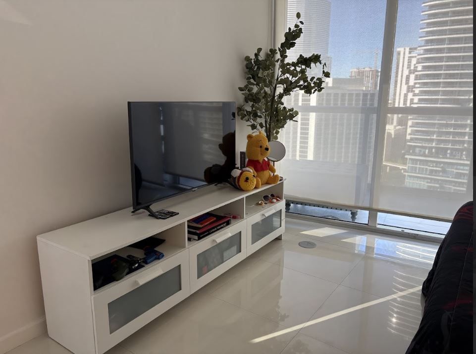 A living room with a television and a teddy bear on a stand.