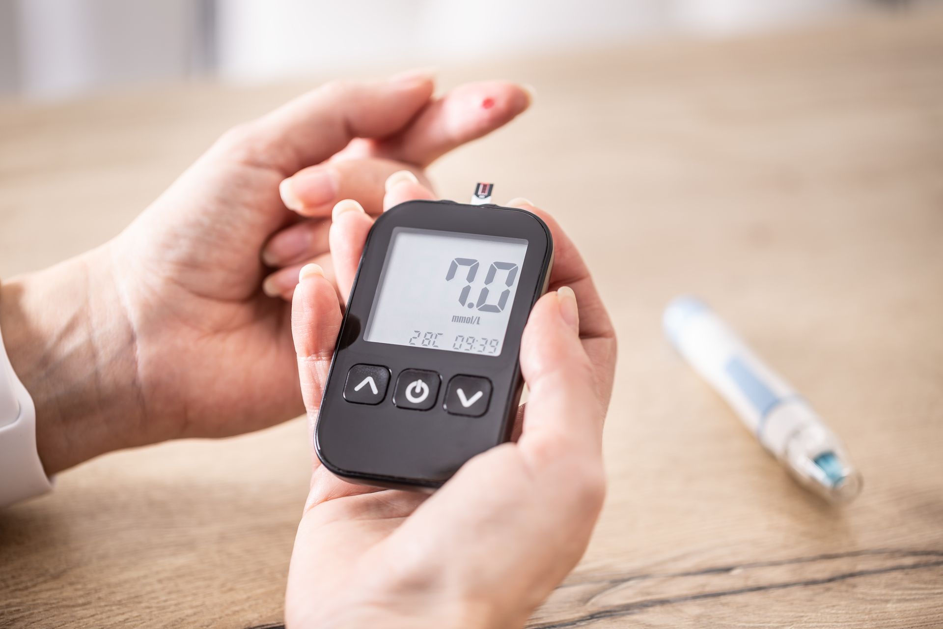 Person testing blood sugar using a glucose meter. The reading is 7.0. Finger with blood drop visible.