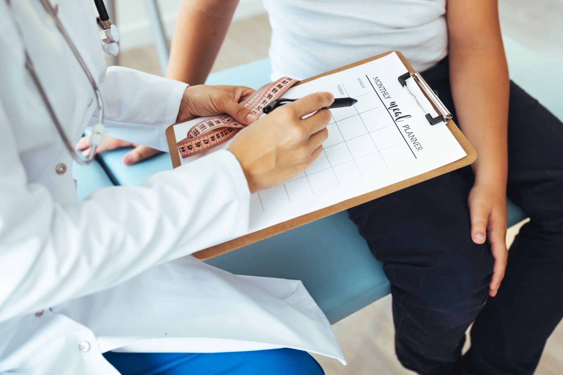 Doctor in white coat reviews notes on clipboard with patient; medical setting.