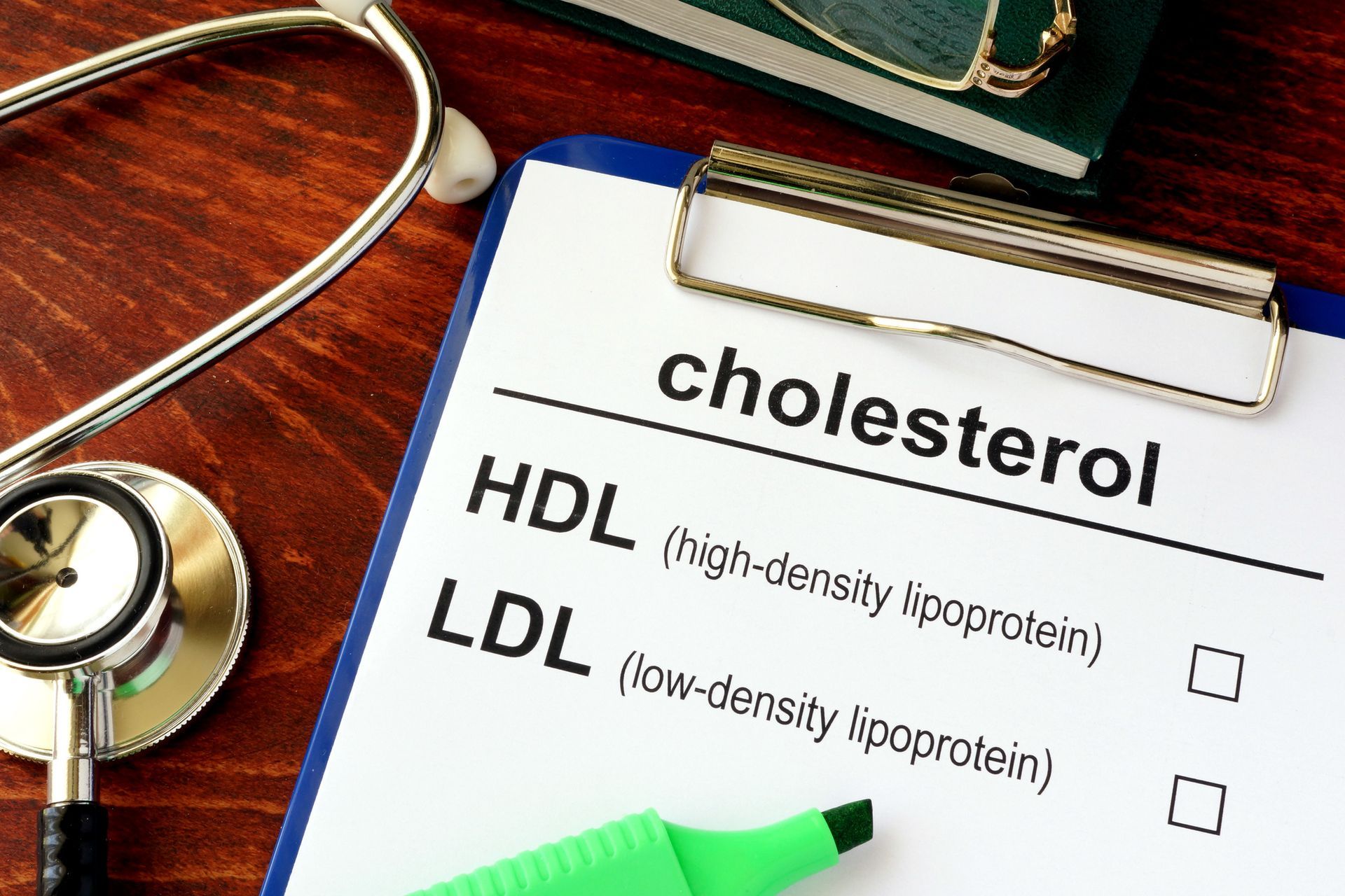 Clipboard with cholesterol test details next to a stethoscope and book.