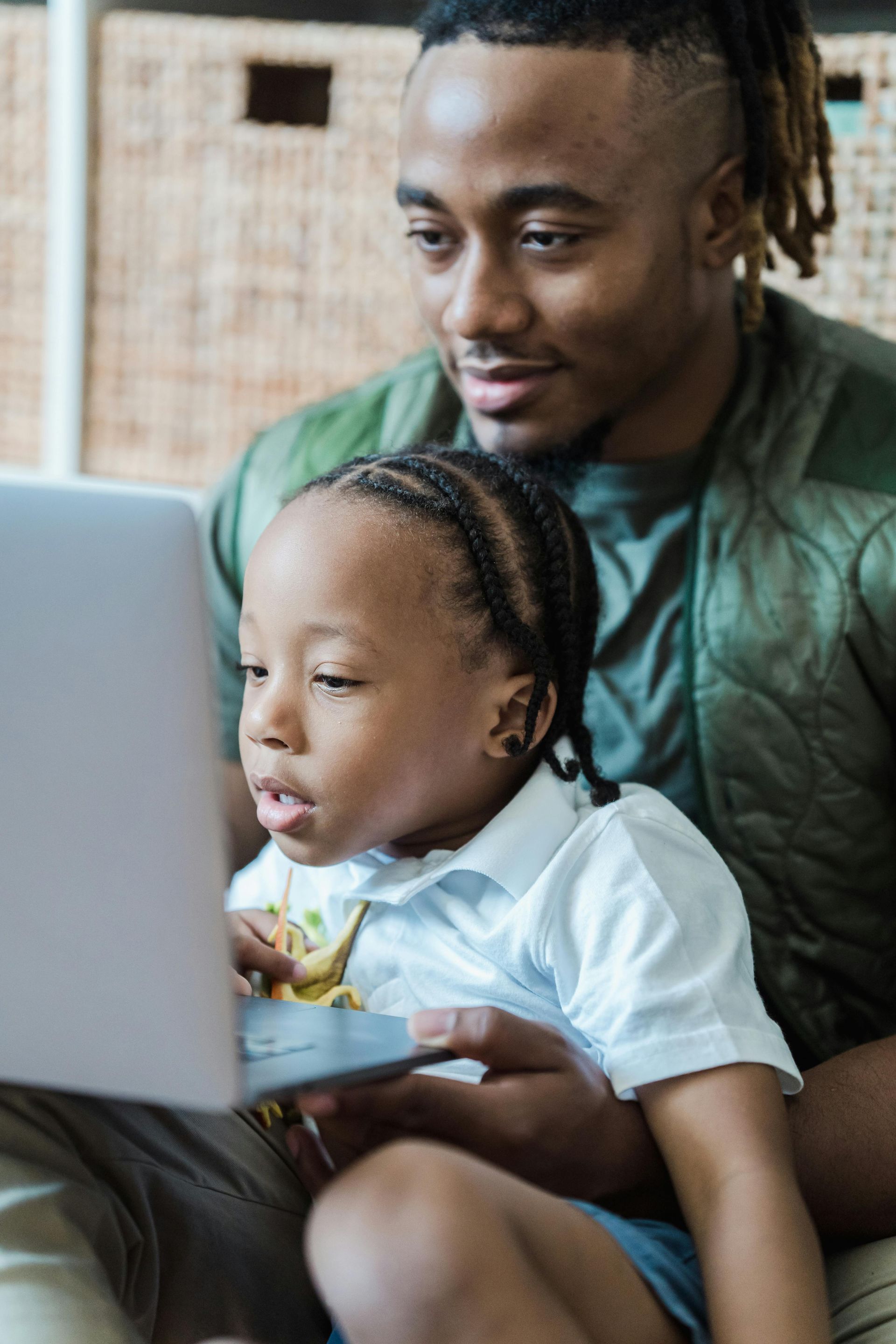Man and child looking at laptop. Child points to screen, man smiles.