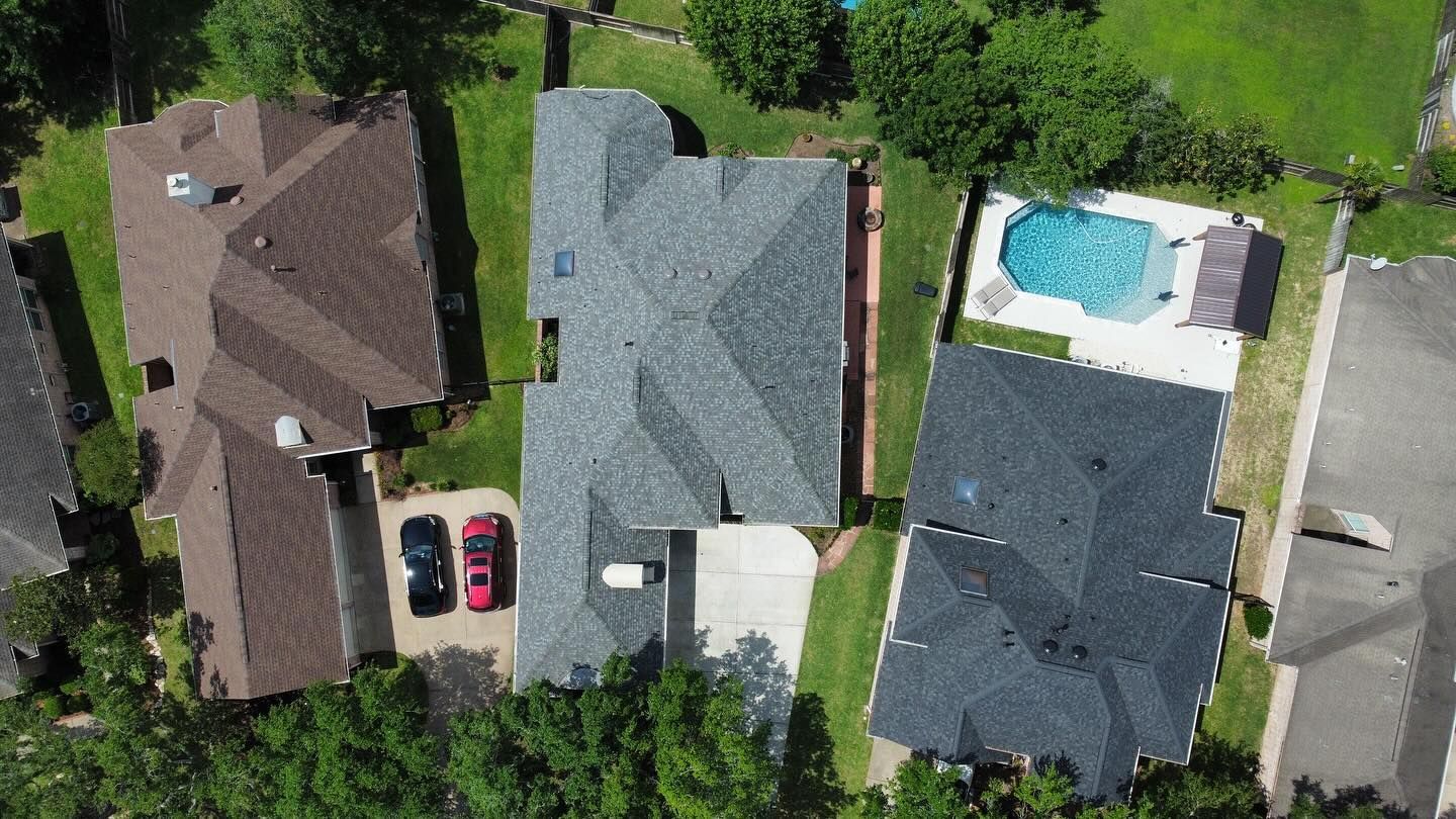 Overhead view of houses with rooftops in shades of brown and gray, with driveways and a pool.