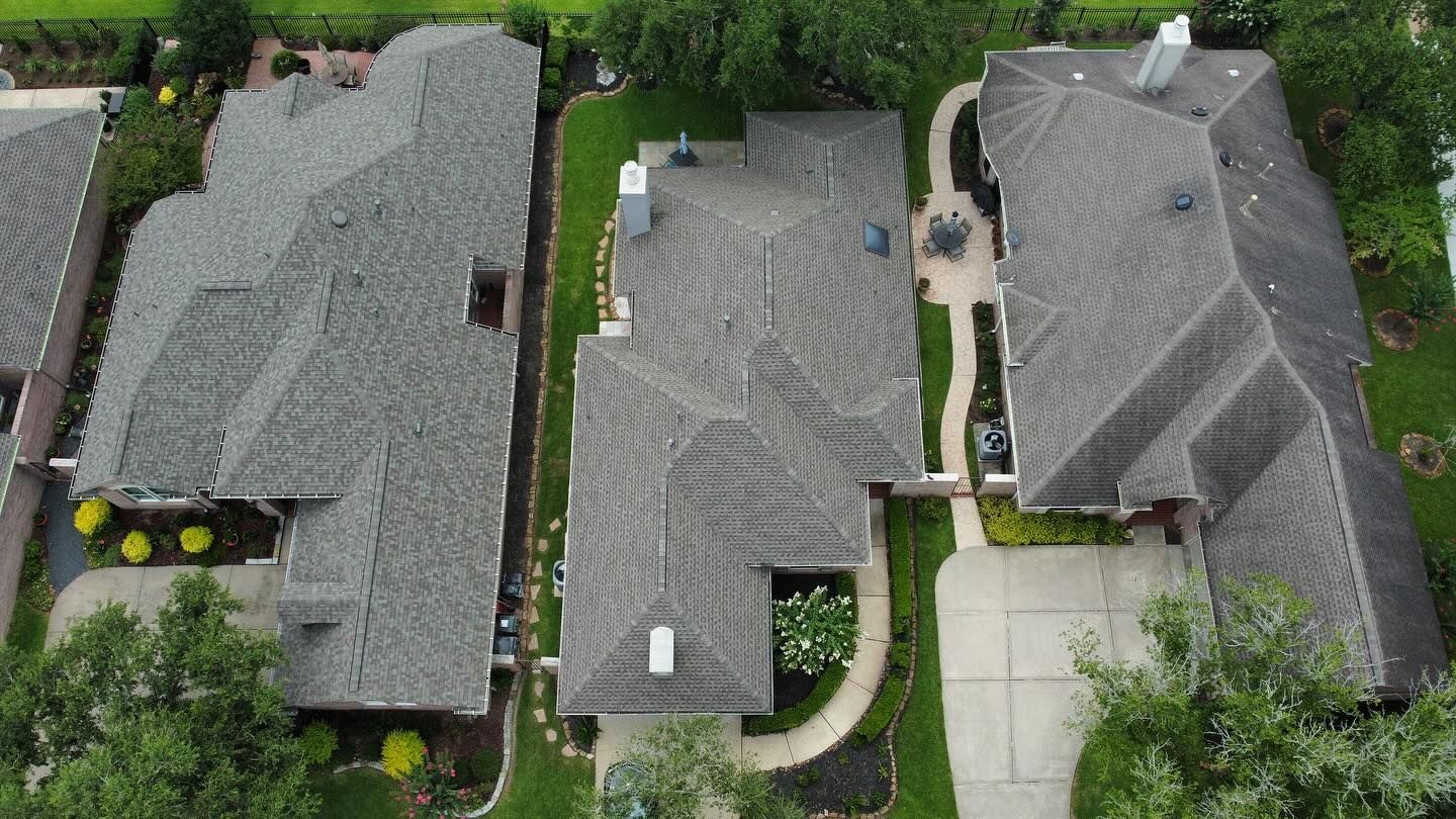 Aerial view of three gray-roofed houses with green lawns and trees.