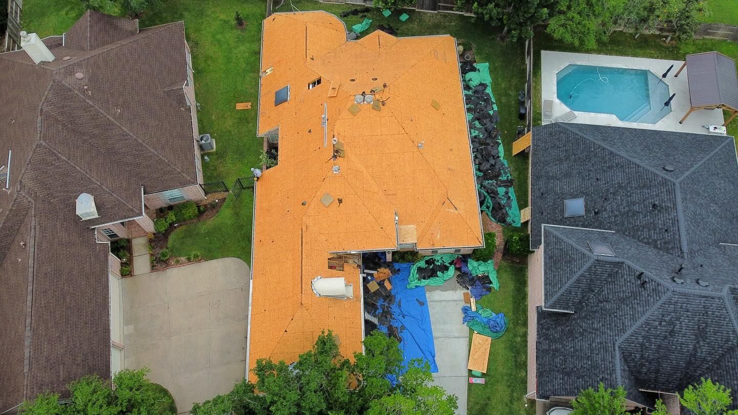 Aerial view of a house with severe roof damage from a storm, debris scattered in the yard.