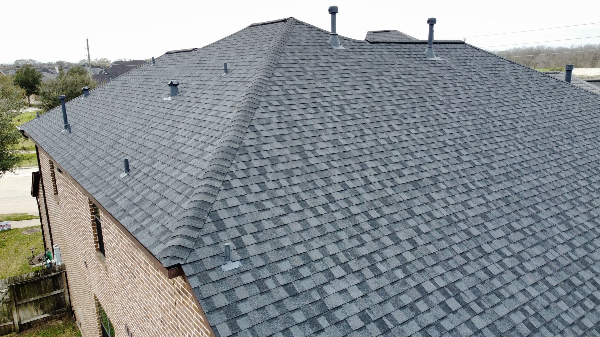 Dark gray asphalt shingle roof on a two-story brick house with multiple chimneys.