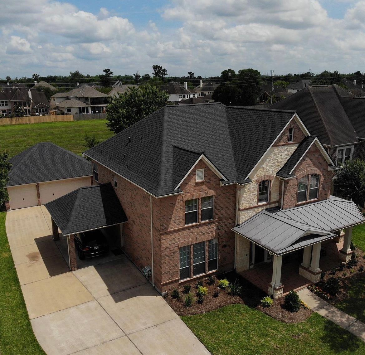 Two-story brick house with a dark roof and attached carport. Green grass surrounds it.