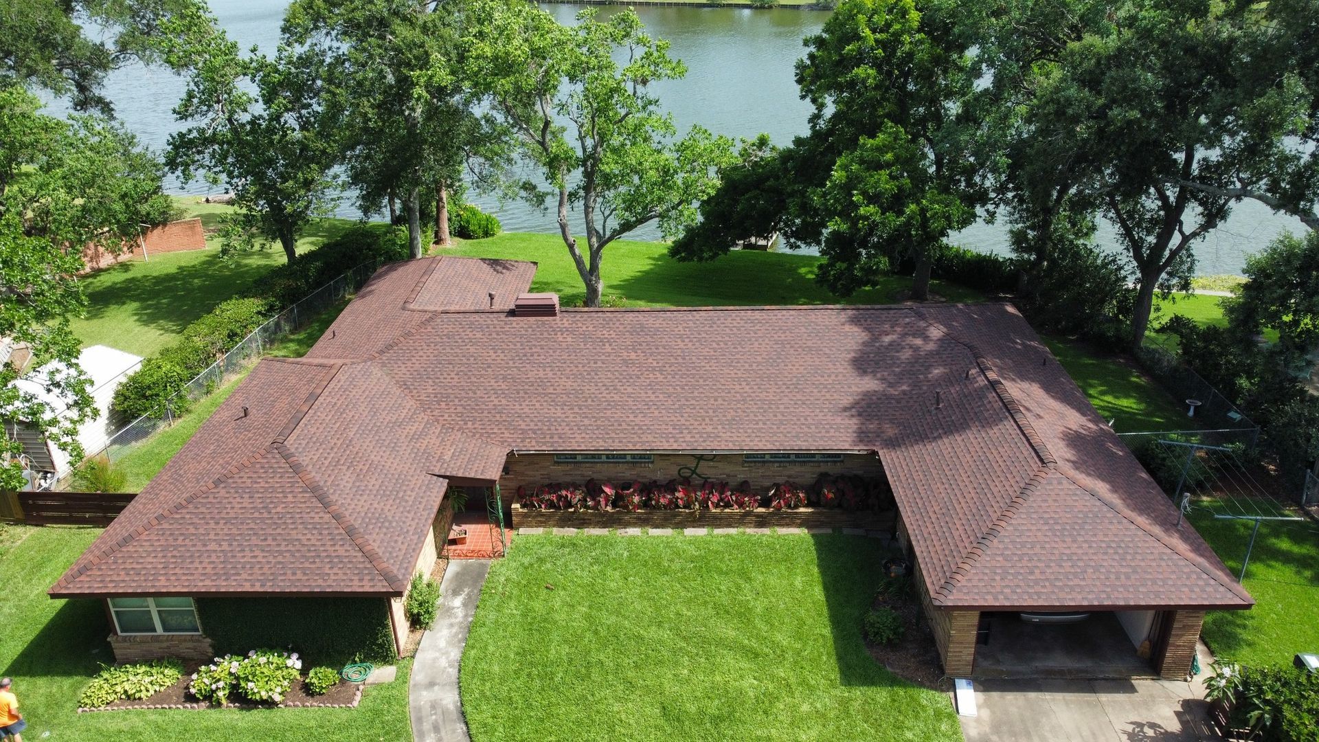 Brown-roofed house with green lawn, trees, and waterway in background.