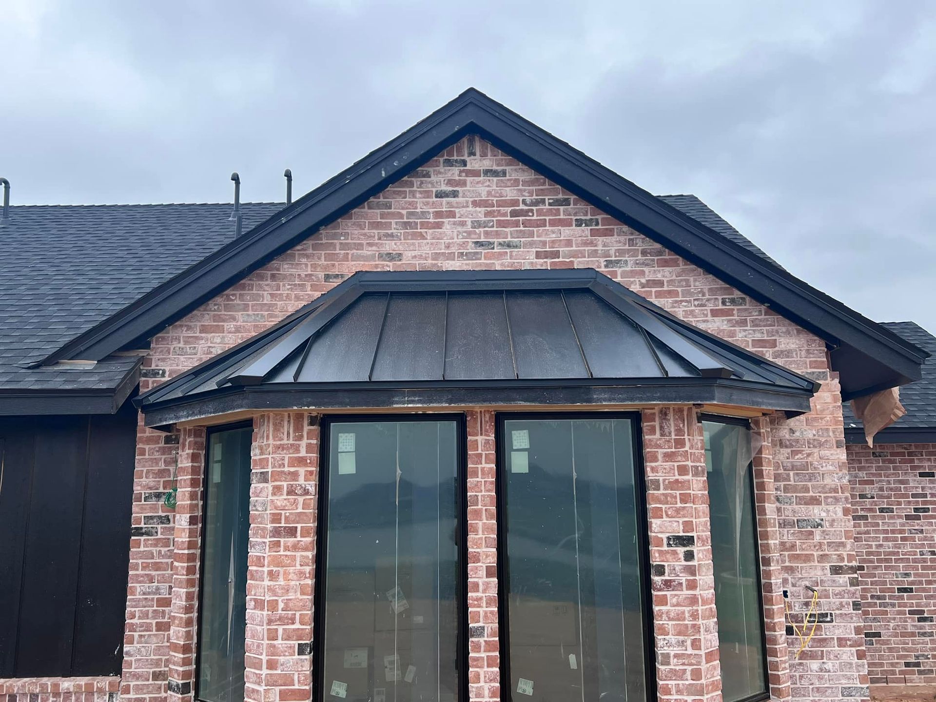 Brick house exterior with dark trim and large windows. Black roof and gray sky.