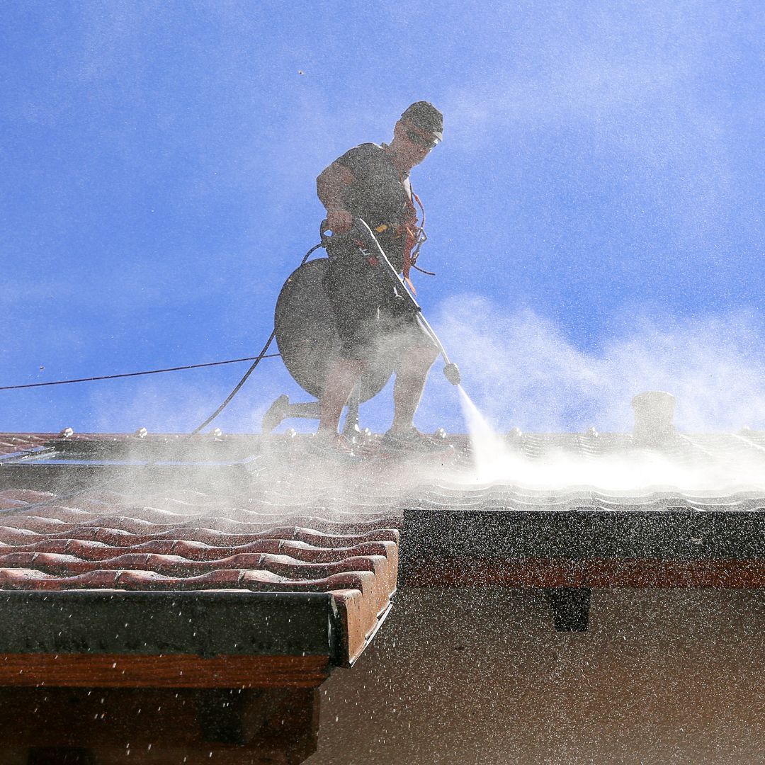 Man pressure washing a tiled roof on a sunny day.