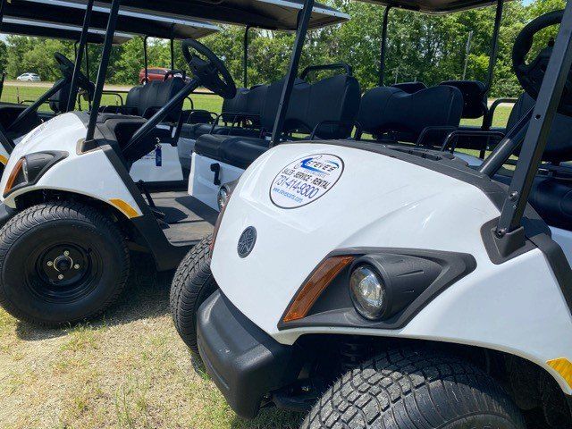Two white golf carts are parked next to each other on a grassy field.