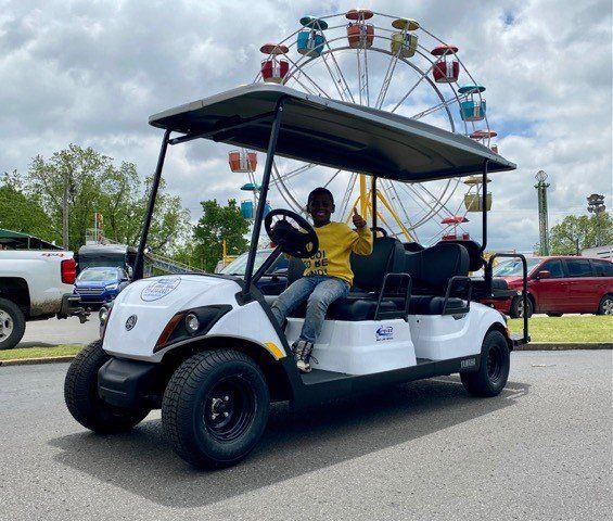 A boy is sitting in a golf cart in front of a ferris wheel.