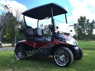 A red and black golf cart is parked on a lush green field.
