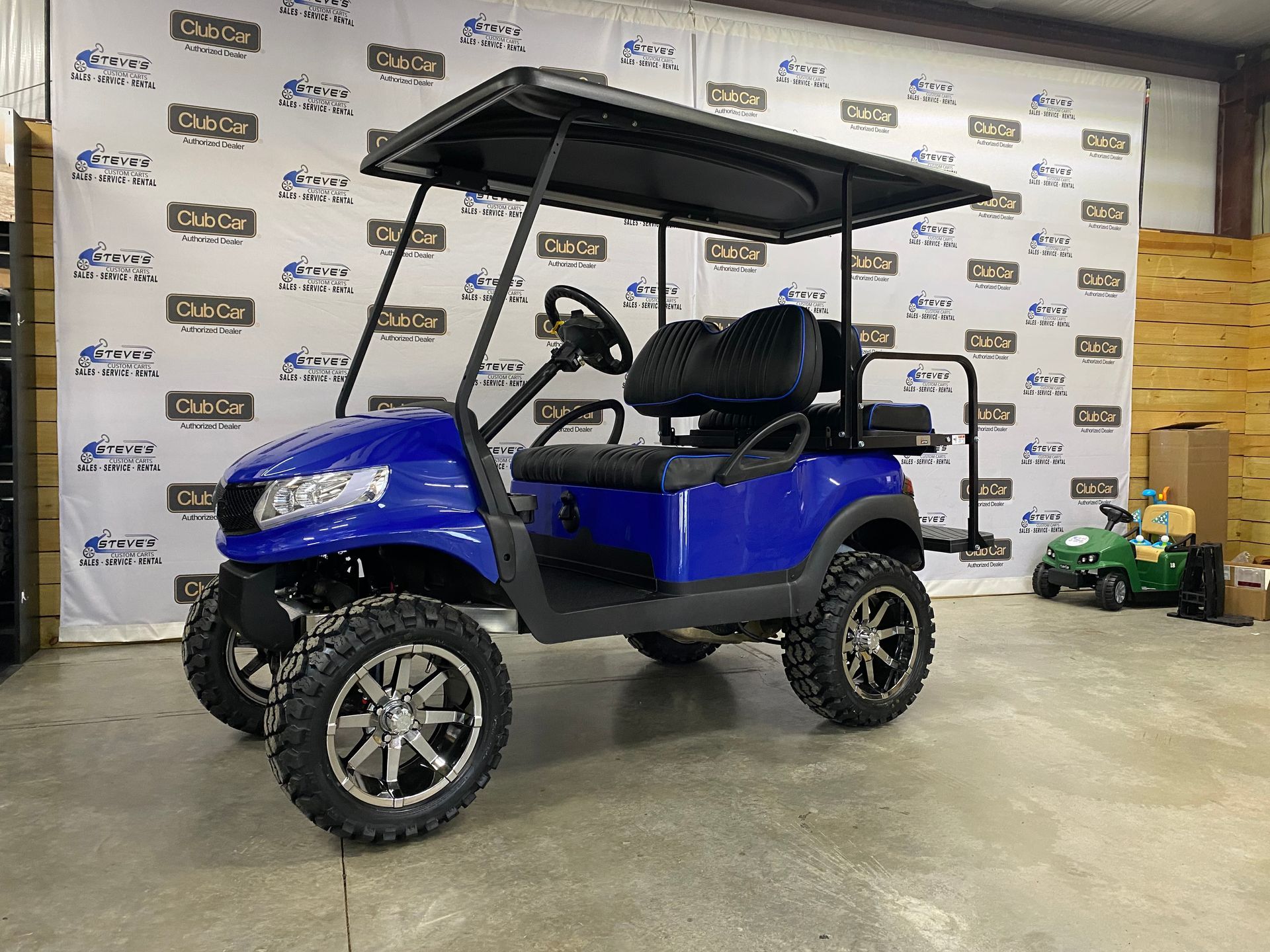 Blue golf cart with black roof and large tires, parked in a warehouse.