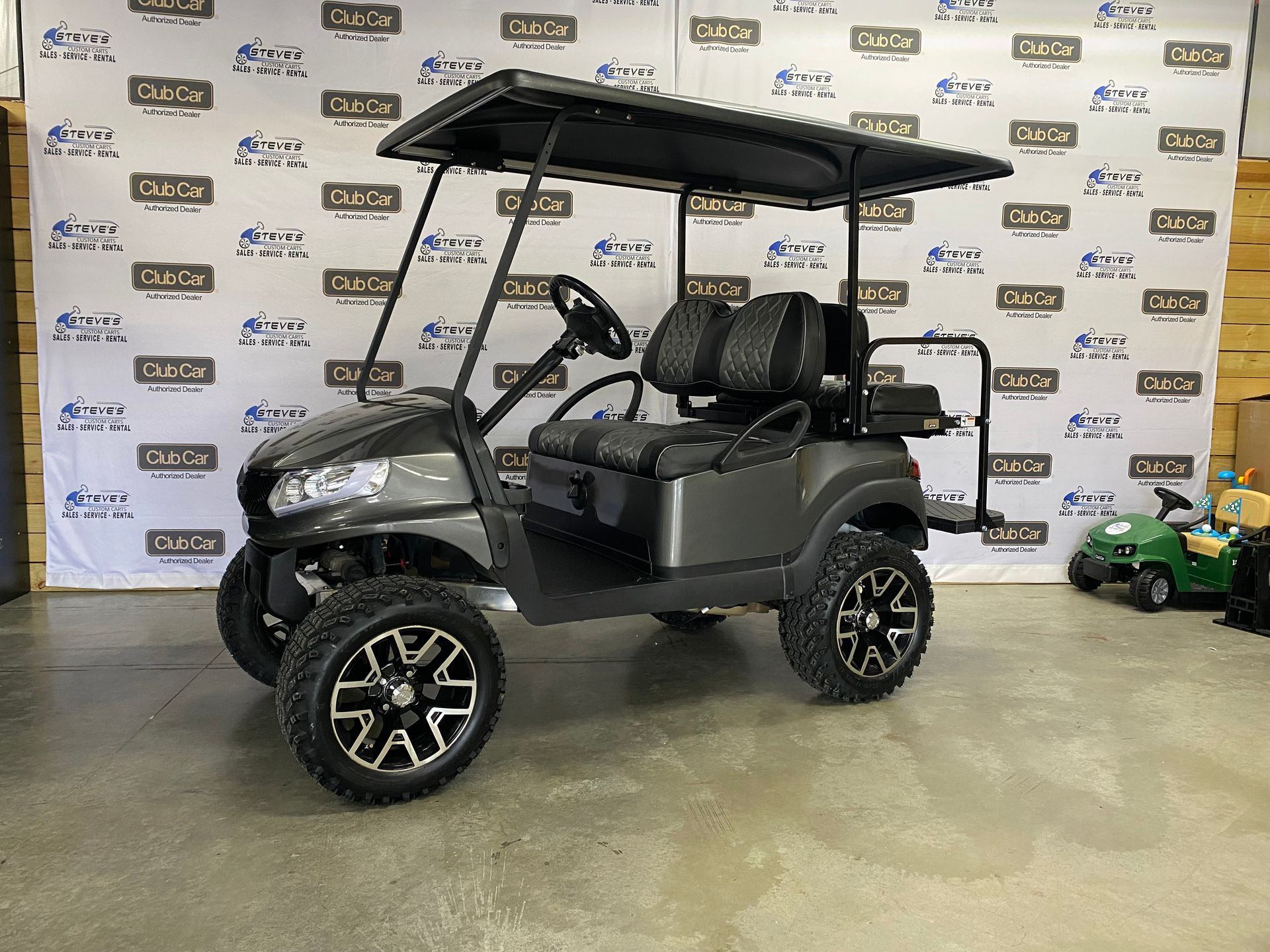 Dark gray golf cart with black roof and wheels, parked indoors.