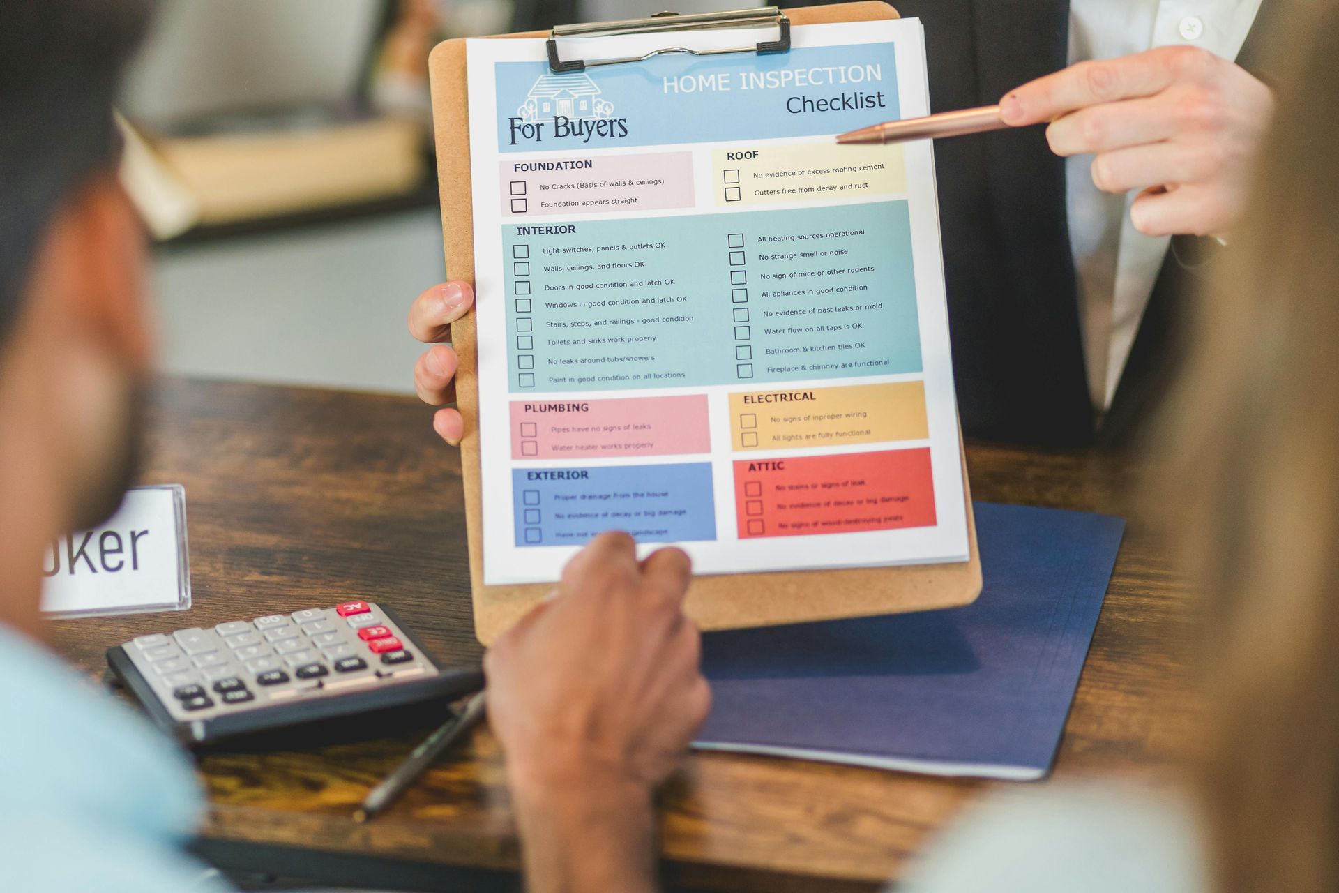 A person in a business suit points to a colorful checklist on a clipboard being held by another individual at a desk.