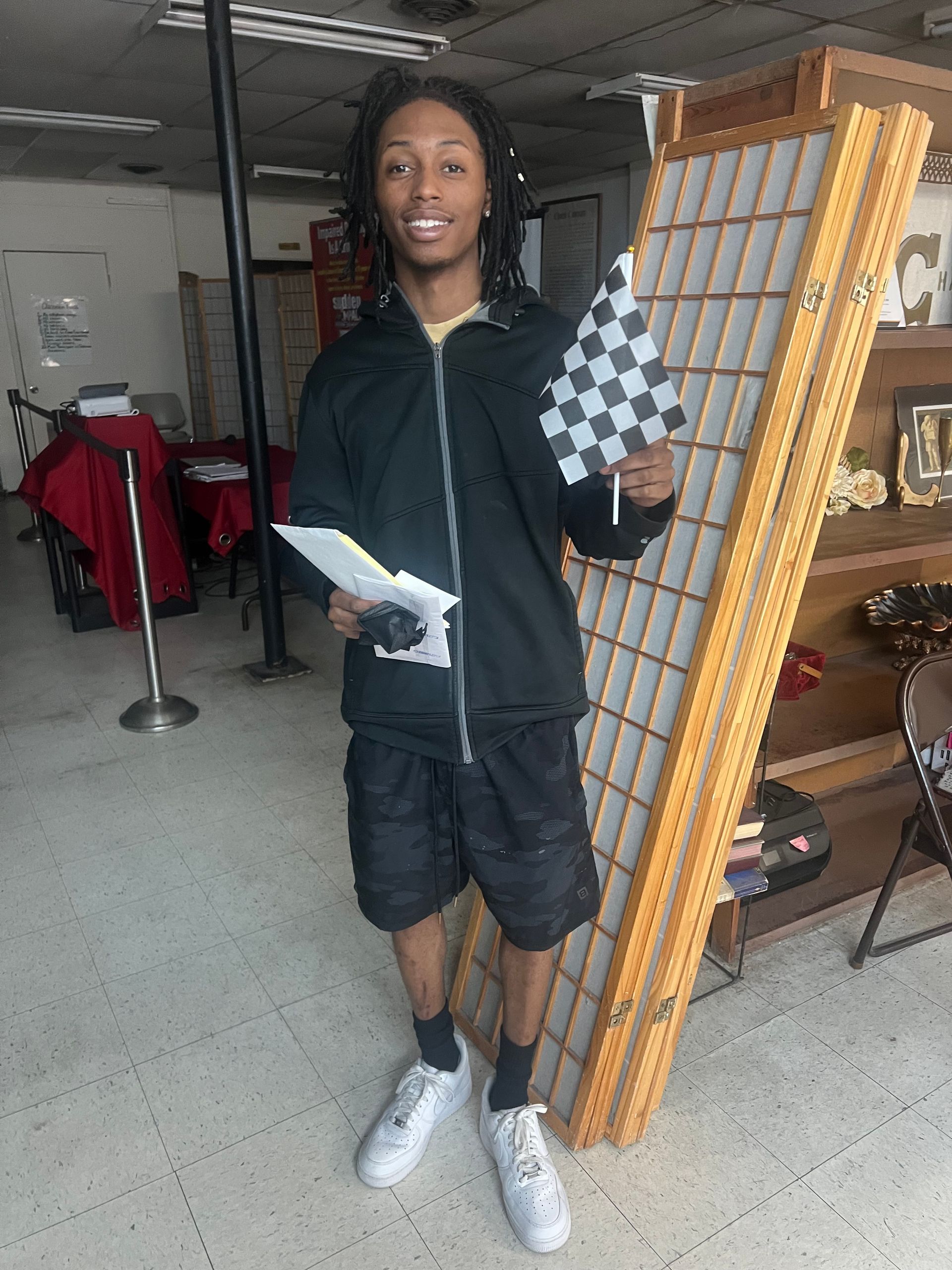 A man in a black jacket is holding a checkered flag and a piece of paper.